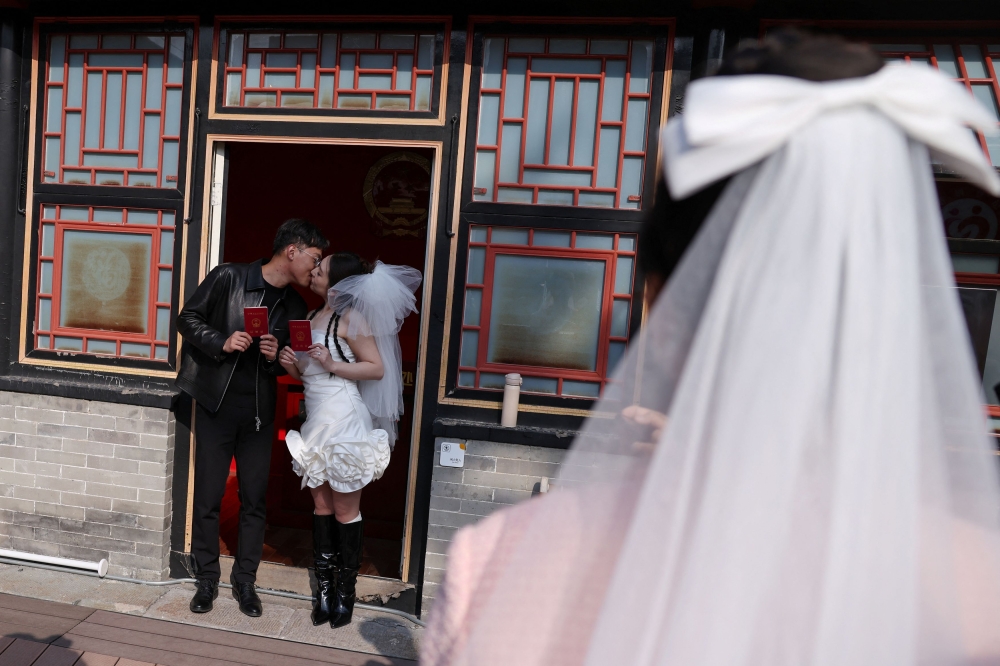 A newlywed couple pose for pictures with their marriage certificates after they registered at the Huguo Guanyin Temple, in Beijing, China, October 28, 2025. — Reuters pic 