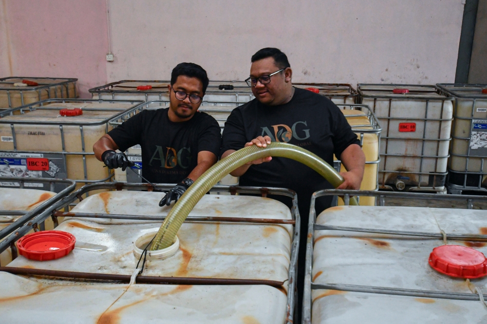 Muhammad Arif Arman Suddin (right) and Mohammad Azhan Shamsu Anuar funnel used cooking oil at the Arjuna Dharma Global Management Office, Kadok in Kota Bharu on November 9, 2025. — Bernama pic
