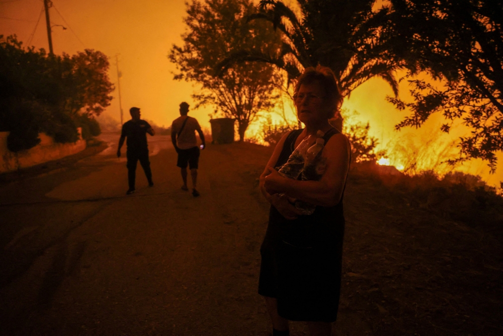 A local resident holds bottles of water next to a wildfire burning in the village of Latas, in southern Greece, June 22, 2024. — Reuters pic