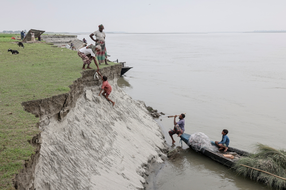 Kosim Uddin, 50, receives fish from a boy after making a purchase, on an island in the Brahmaputra River where he recently relocated his house due to erosion, in Kurigram, Bangladesh, October 29, 2025. — Reuters pic 