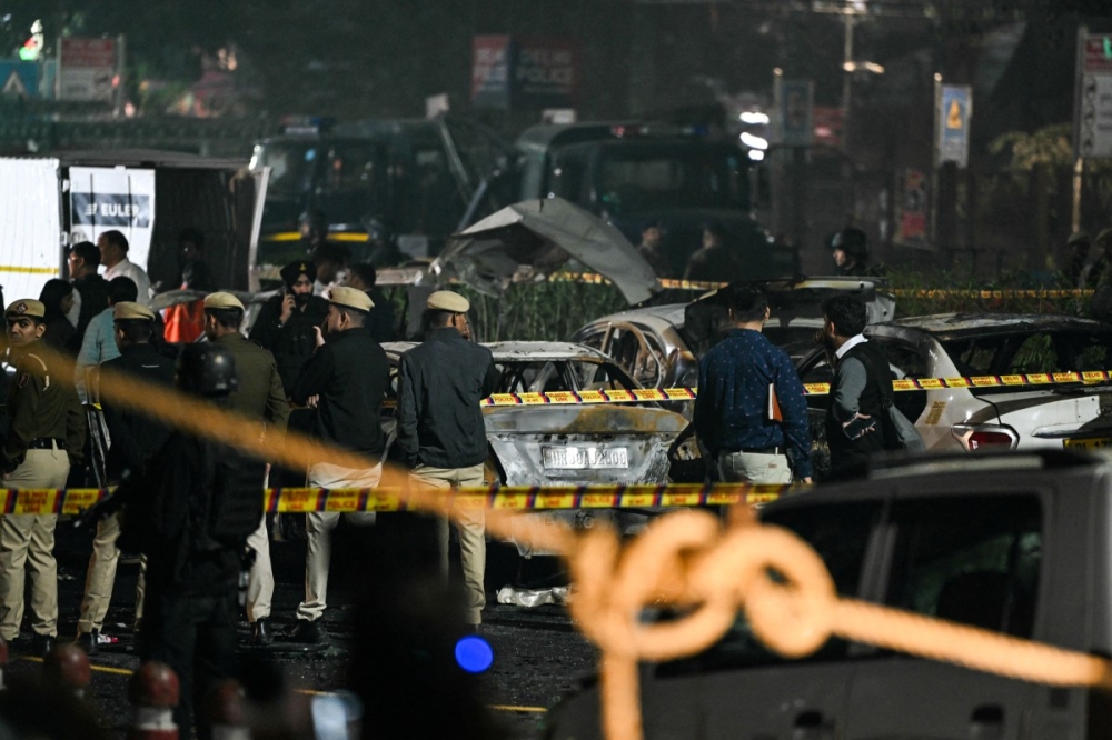 Police and security personnel stand behind the safety cordons delimiting the blast site as they inspect charred vehicles following an explosion near the Red Fort, in the old quarters of Delhi, November 10, 2025. — AFP pic