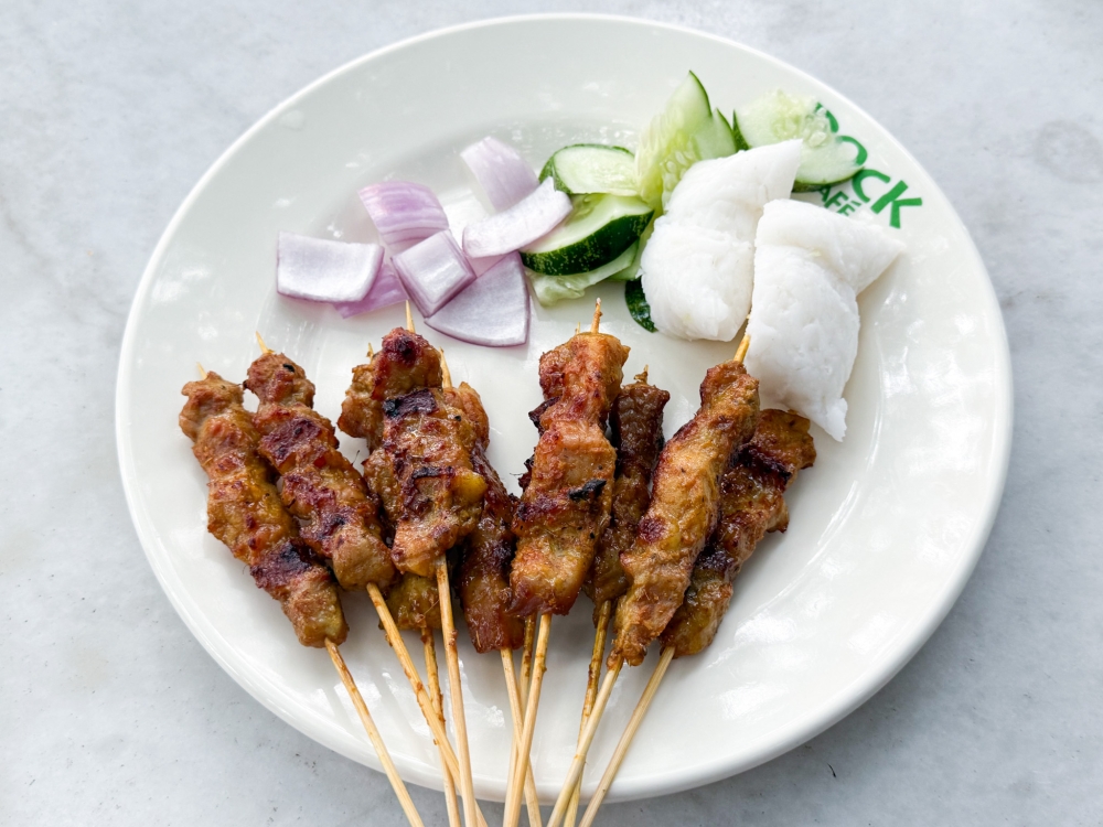 Glorious juicy grilled pork satay is served with ‘nasi impit’, cucumber and red onions. — Picture by Lee Khang Yi
