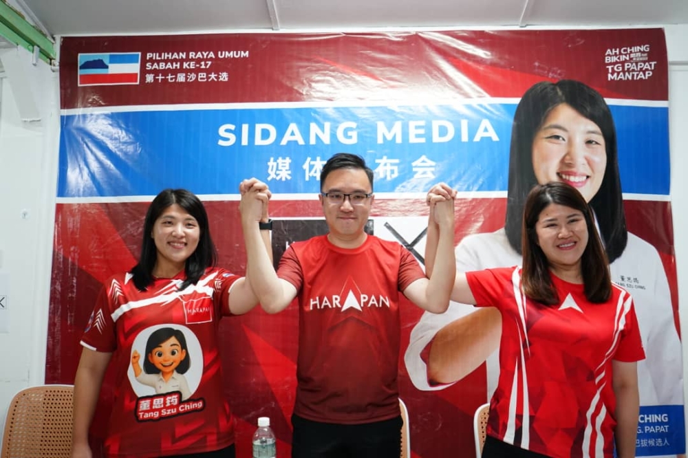 Phoong (centre) raises the hands of Pakatan Harapan candidates for the Tanjung Papat and Elopura seats, Tang Szu Ching (left) and Vivian Wong. — Daily Express pic
