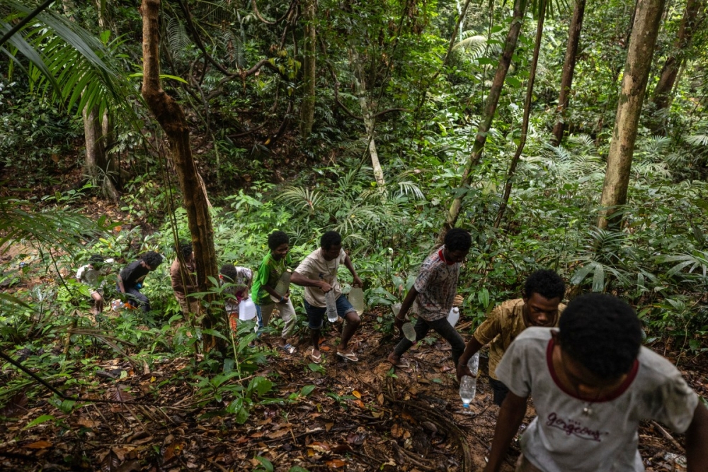 Maniq teenagers return from collecting water from a natural spring in the forest nearby to their camp in Phatthalung in southern Thailand. — AFP pic