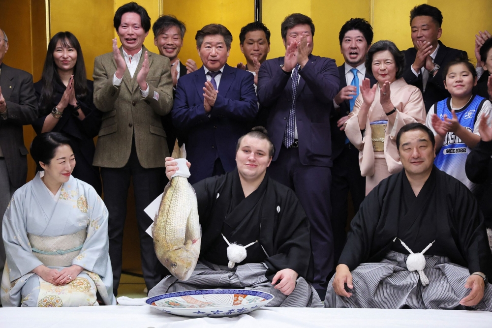 Ukrainian sumo wrestler Danylo Yavhusishyn (front C), also known by his Japanese ring name Aonishiki Arata poses with a seabream to celebrate after winning the Grand Sumo Tournament in Kurume city of Fukuoka Prefecture on November 23, 2025. — AFP pic