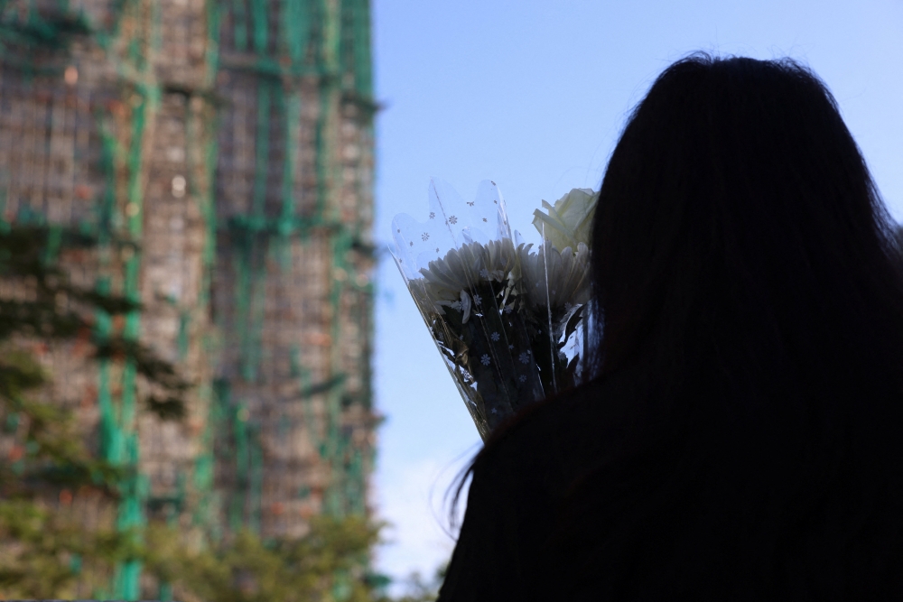 A woman holds flowers at a makeshift memorial near Wang Fuk Court housing estate to pay tribute to victims of the deadly fire at the Wang Fuk Court housing complex, in Tai Po, Hong Kong, China, November 29, 2025. — Reuters pic