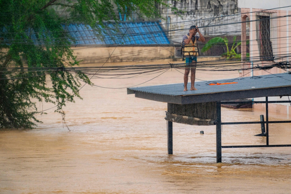 A man stands on a roof next to high flood waters in Hat Yai in Thailand’s southern Songkhla province on November 26, 2025. — AFP pic
