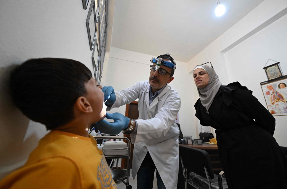 Dr Hussam Jamous, a 55-year-old, an ear, nose and throat specialist who fled with his family at the start of the siege in 2012, examines a patient at his clinic in Daraya. — AFP pic 