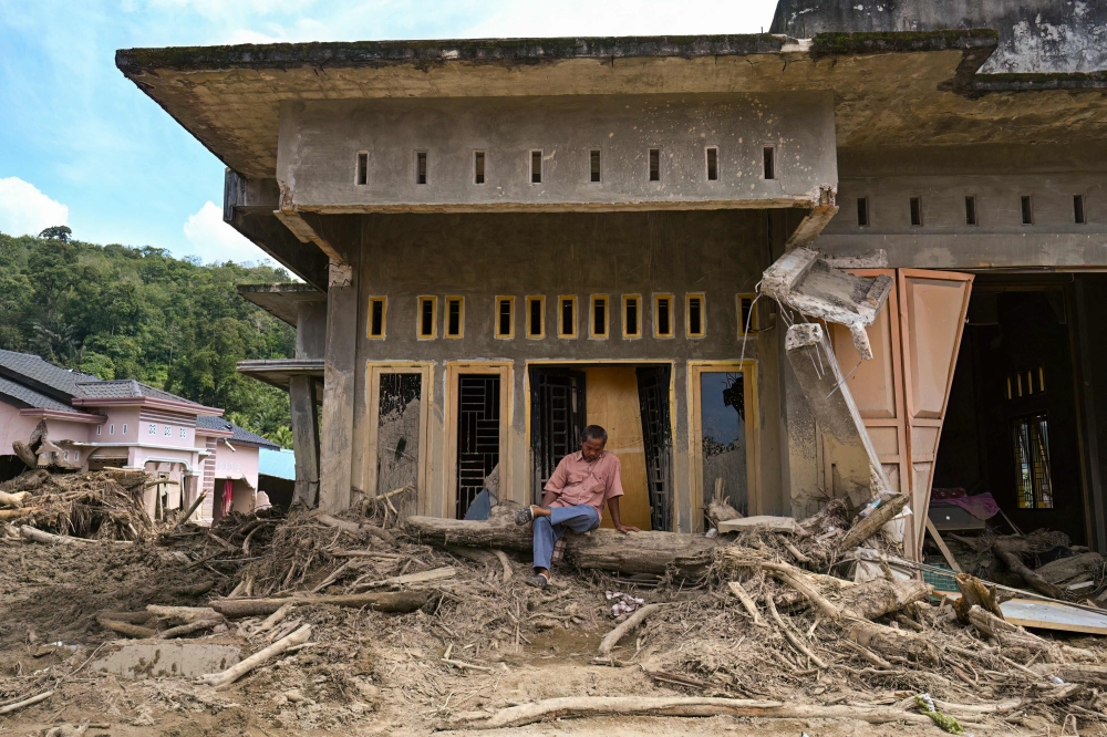 A villager sits in front of his house damaged by a flash flood in Garoga, North Sumatra province on December 4, 2025. — AFP pic