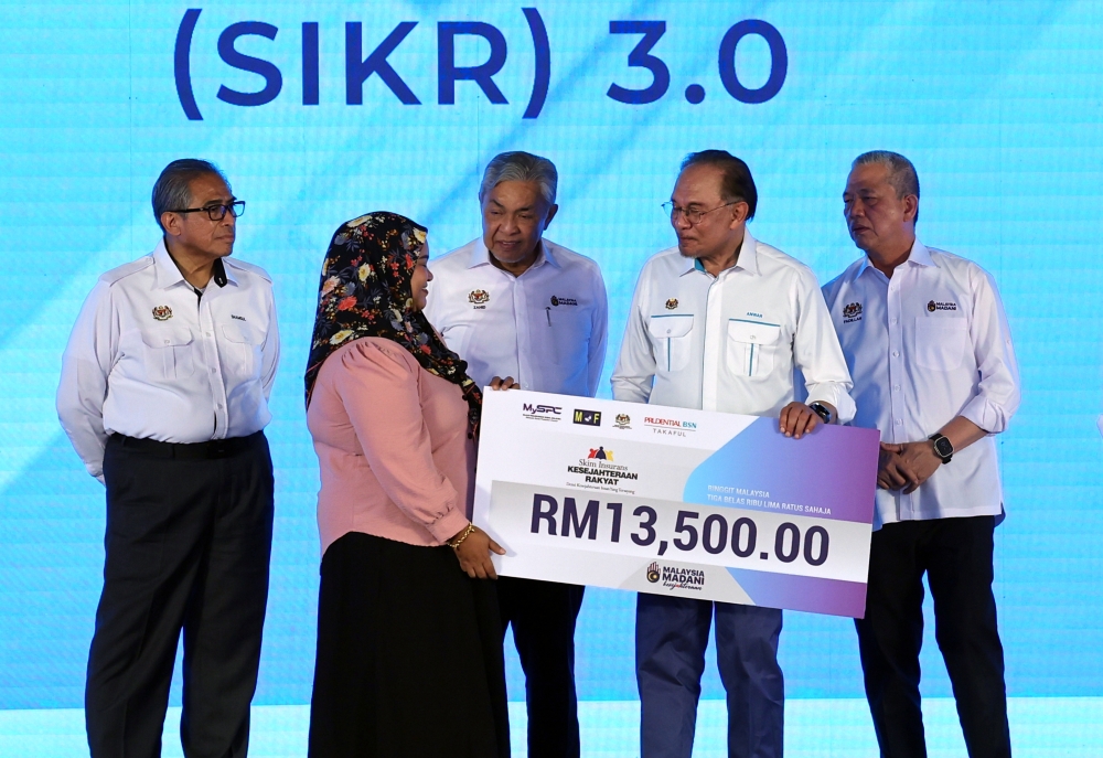 Prime Minister Datuk Seri Anwar Ibrahim (second from right) presents the People’s Welfare Insurance Scheme (SIKR) 3.0 to a recipient representative at the closing ceremony of the ‘Rancakkan Madani Bersama Malaysiaku programme’ at Dataran Putrajaya on December 7, 2025, accompanied by Deputy Prime Ministers Datuk Seri Dr Ahmad Zahid Hamidi (centre) and Datuk Seri Fadillah Yusof (right), and Chief Secretary to the Government Tan Sri Shamsul Azri Abu Bakar (left). — Bernama pic