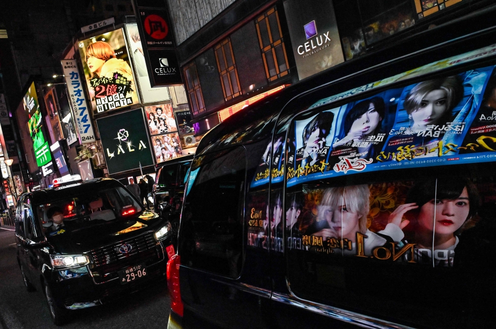 This photo taken on March 31, 2025 shows advertisements for entertainment clubs reflected in the window of a passing car, along a street in the red-light entertainment area of Kabukicho in the Shinjuku district of Tokyo. — AFP pic