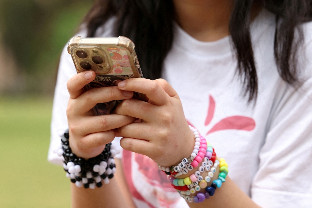 A girl poses holding her phone in Sydney, Australia, on November 22, 2025, after an interview discussing Australia’s social media ban for users under 16, which is scheduled to take effect on December 10. — Reuters pic