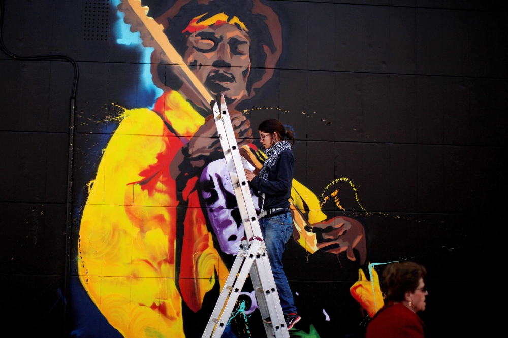 A woman paints graffiti of the rock star Jimi Hendrix, on the wall of a music shop in Malaga, southern Spain, February 18, 2015. — Reuters pic