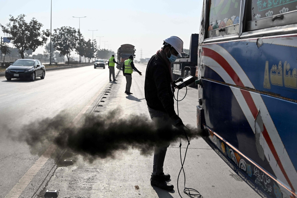 Pakistani technician Waleed Ahmed (right) examines a vehicle to test its emissions on road on December 10, 2025 as Islamabad grapples with self-inflicted smog. — AFP pic