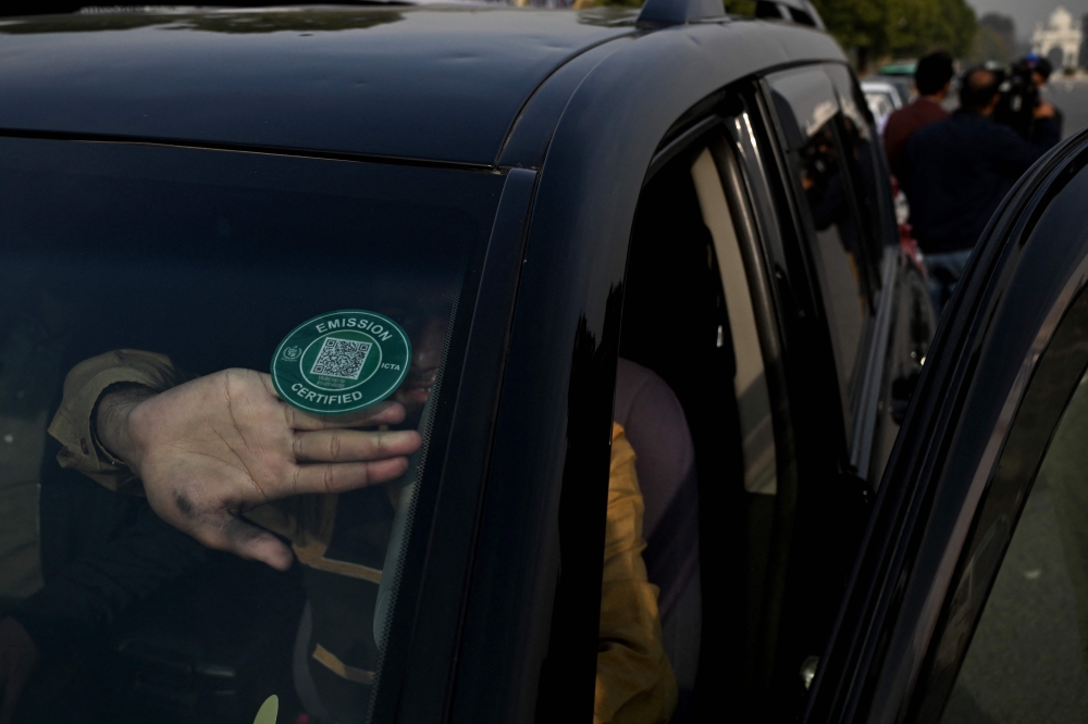A technician pasting a certified sticker on a car after it cleared an emission test in Islamabad on December 10, 2025 as the Pakistani capital city grapples with smog. — AFP pic