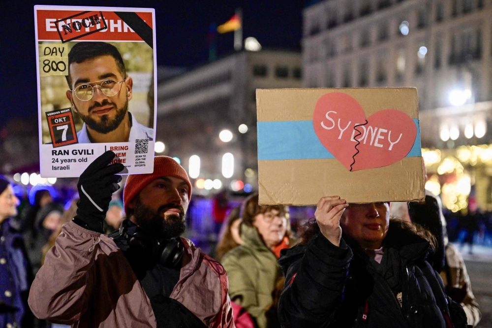 People hold placards during a Hanukkah menorah lighting in Berlin, Germany on December 14, 2025, in solidarity with Australians after the Bondi Beach shooting. — AFP pic