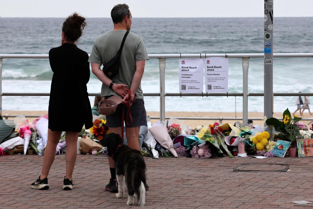 A couple pauses at floral tributes on Bondi Beach to pay respects to the victims of the Sydney shooting December 16, 2025. — AFP pic 