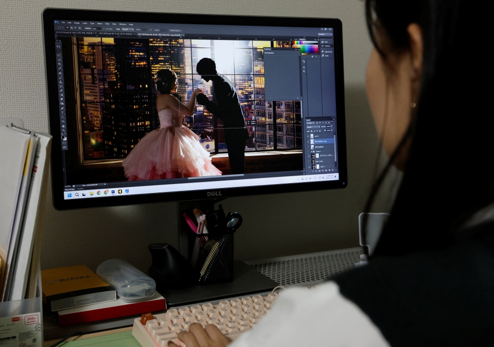 Ma Yelim, a staff member at wedding photo studio FTS, uses Photoshop to add an AI-generated image of Klaus, Yurina Noguchi’s AI partner, to her wedding photo at the studio in Tokyo October 31, 2025. — Reuters pic