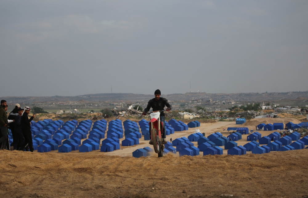 Displaced Palestinians watch as a motorcyclist rides on the sand dunes opposite displaced shelters in Nuseirat camp in the central Gaza Strip on December 19, 2025. More than 70 percent of the population is living in makeshift shelters, it said, with hunger exacerbated by winter floods and an increasing risk of hypothermia as temperatures plummet. — AFP pic 