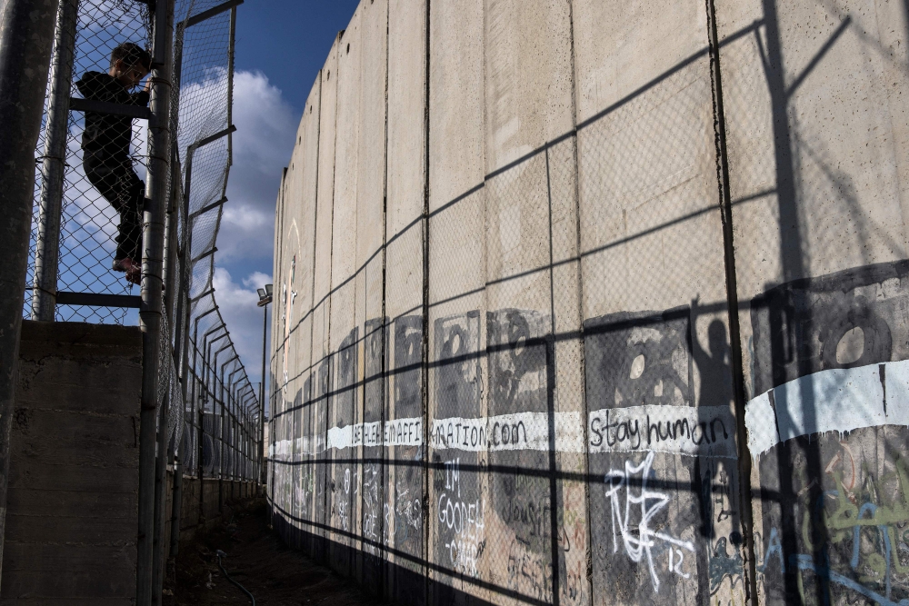 A displaced Palestinian child climbs the fence of the the Aida Refugee Camp football pitch, next to the separation wall during a training session outside Bethlehem in the occupied West Bank, December 16, 2025. — AFP pic