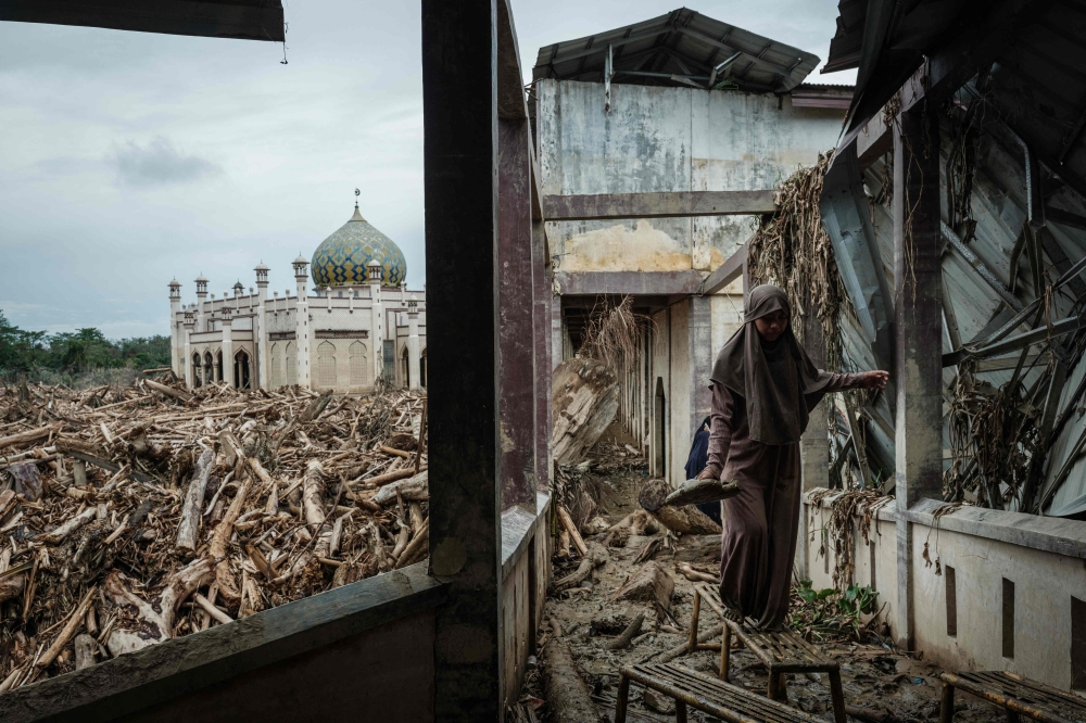 A student from Medang balances on a bench to avoid thick mud, as uprooted trees from a flash flood lie strewn across Darul Mukhlisin Islamic Boarding School and its mosque in Aceh Tamiang, Northern Sumatra, on December 14, 2025. — Bernama pic