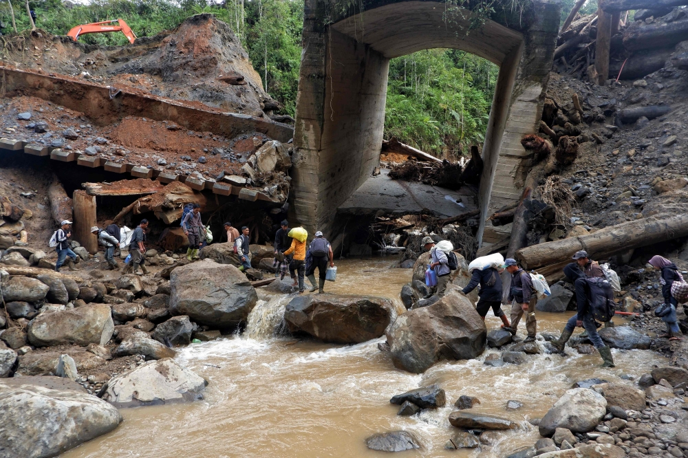 On December 13, 2025, people cross a landslide site in Bener Meriah, Aceh, where a road collapsed after flash floods three weeks earlier. — Bernama pic