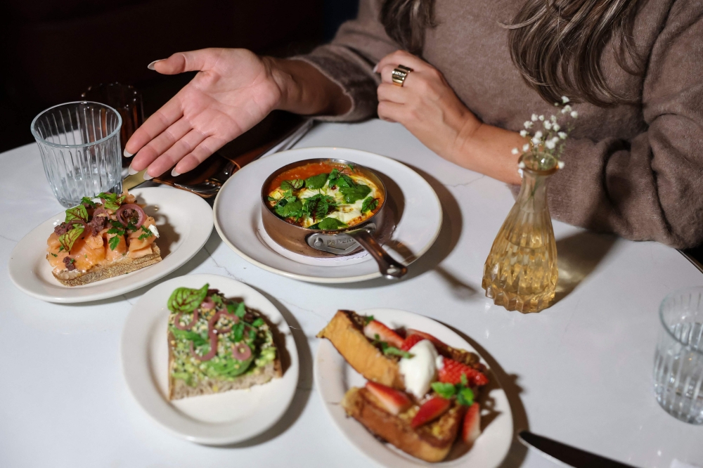 A patron poses at a table with half-sized portions of the brunch tasting at Le Petit Village restaurant on December 10, 2025 in New York City. — AFP pic