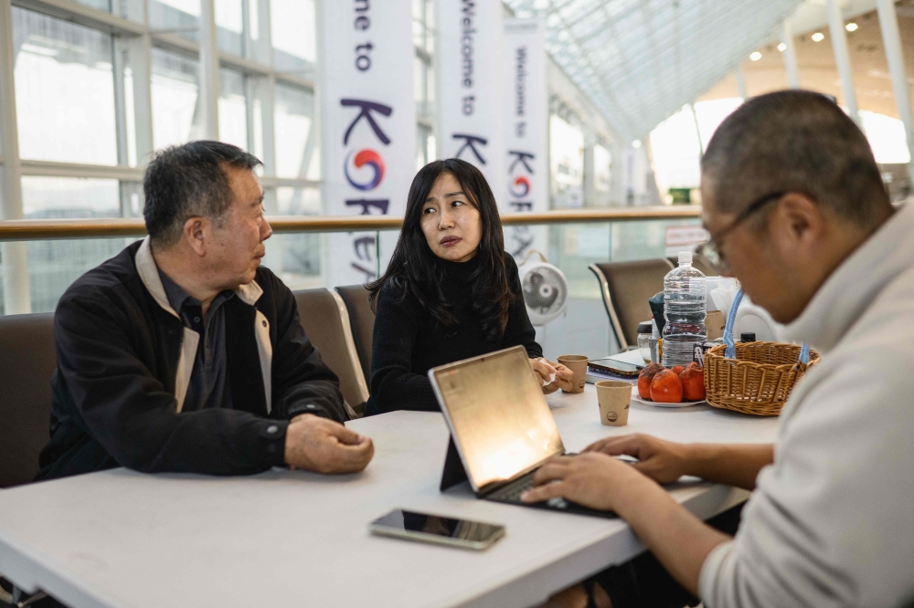 In this photo taken in the departures hall of Muan International Airport on December 14, 2025, Lee Hyo-eun (C), who lost her daughter Ye-won, speaks to Park In-wook (L) who lost lost five loved ones; his wife, daughter, son-in-law and two young grandchildren, in the Jeju Air Flight 2216 plane crash on December 29, 2024. 