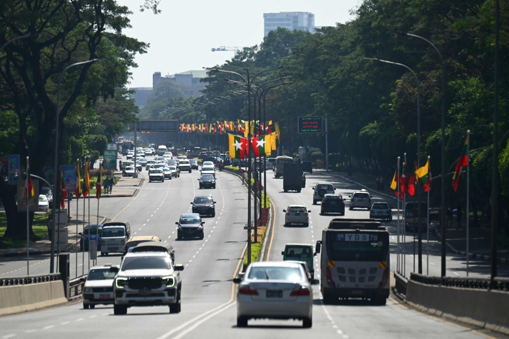 Vehicles drive on a road with the national flags displayed ahead of Myanmar's general election in Yangon on December 23, 2025. — AFP pic