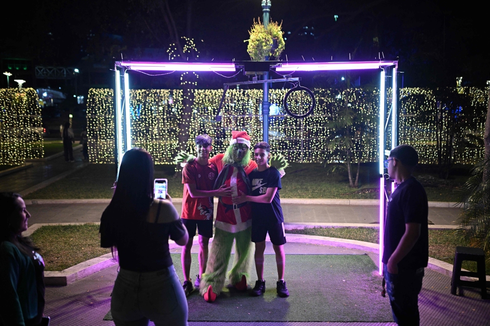 People pose for pictures with a man dressed as Christmas character ‘the Grinch’ at Los Proceres boulevard in Caracas December 19, 2025. — AFP pic