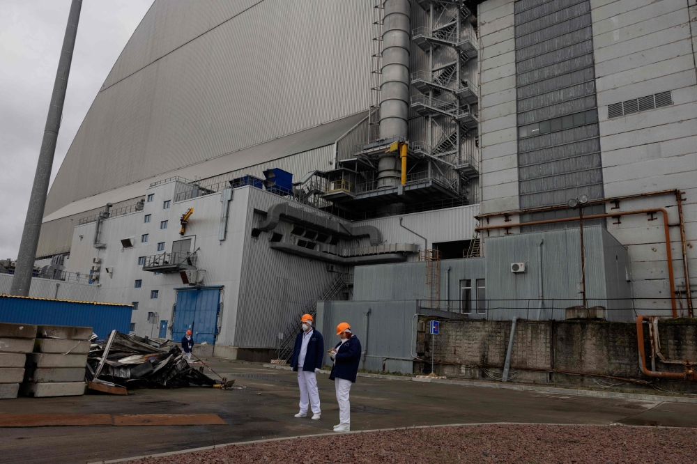 Workers stand next to the debris and damaged panels from the containment vessel following  a drone attack on February 14, 2025, on the New Safe Confinement (NSC) which contains radiation from the remains of reactor 4 of the former Chernobyl Nuclear Power Plant, in Chernoby, on December 22, 2025. — AFP pic