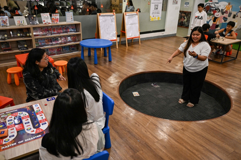 This photo taken on December 9, 2025, shows participants looking at a woman acting as they play Master of Disaster, a board game about disaster preparedness, at a library in Valenzuela, Metro Manila. — AFP pic