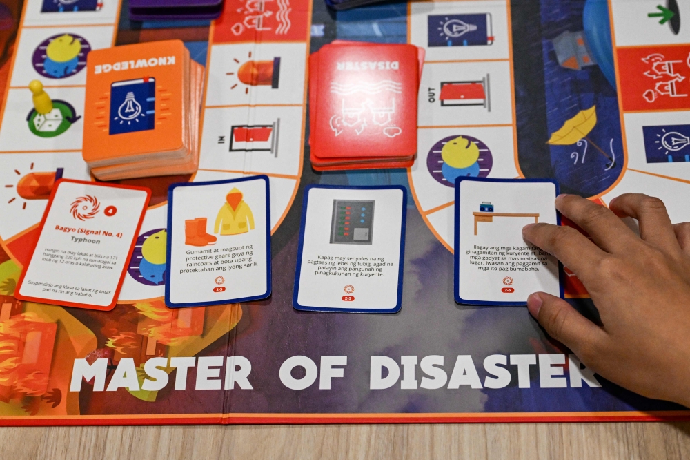 This photo taken on December 9, 2025, shows a participant placing response cards to a playing game that states Tropical Depression Signal No. 4” (L) as they play Master of Disaster, a board game about disaster preparedness, at a library in Valenzuela, Metro Manila. — AFP pic