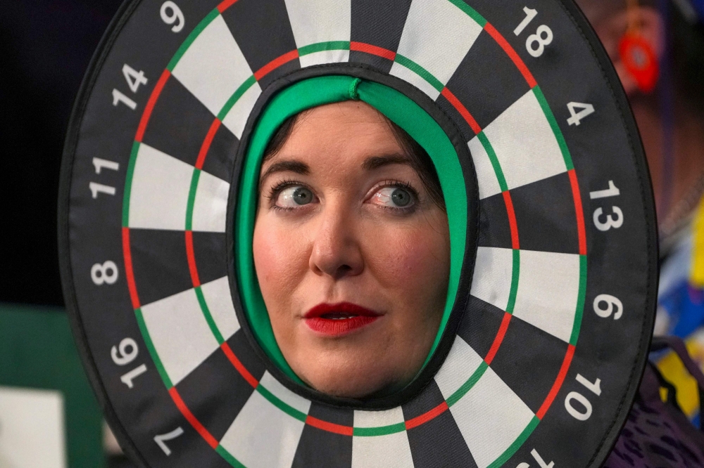 A woman wearing dartboard-themed headgear watches during the World Darts Championship at Alexandra Palace in London December 28, 2025. — AFP pic