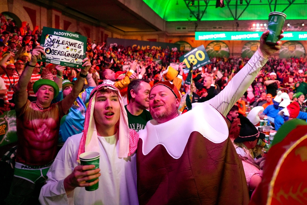 Fans, including one dressed as a Christmas pudding (right), cheer during the World Darts Championship at Alexandra Palace in London December 28, 2025. — AFP pic