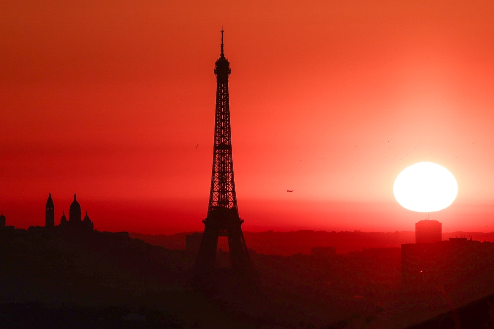 The sun rises by the Eiffel Tower and the Sacre Coeur Basilica ontop of the Montmartre hill in Paris on July 1, 2025, as the city is on red alert for high temperatures, with the top of the Eiffel Tower shut, polluting traffic banned and speed restrictions in place as a searing heatwave gripped Europe. Scientists say human-induced climate change is making such heatwave events more intense, frequent and widespread. — AFP pic 