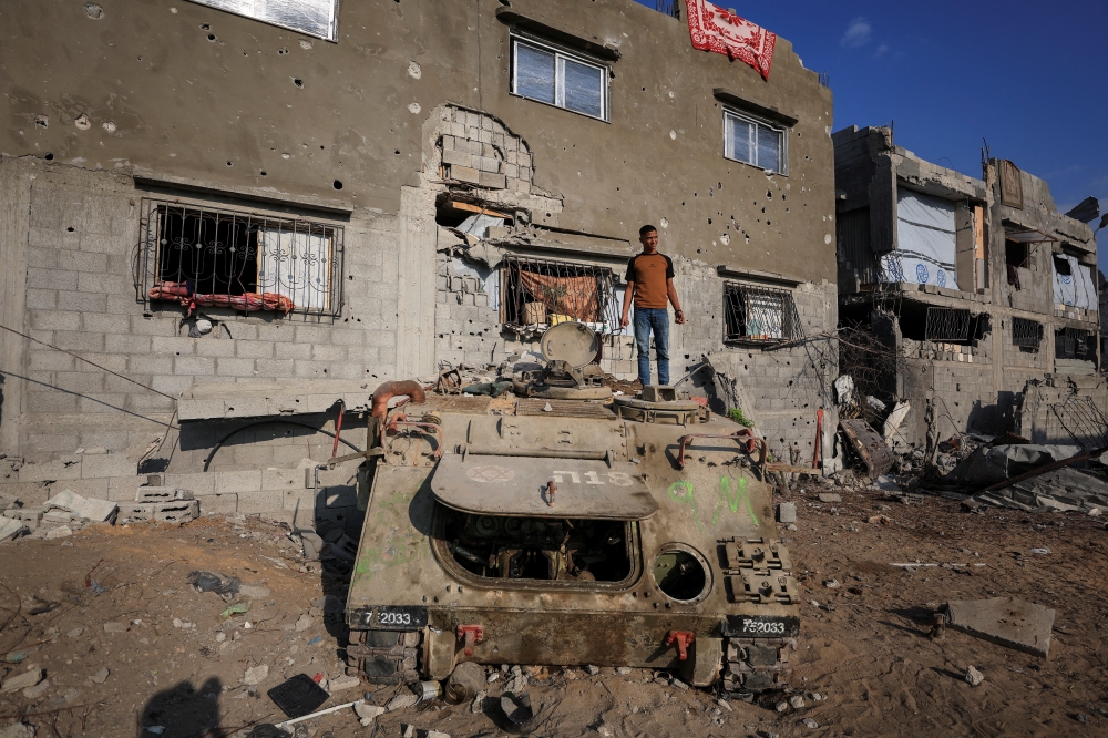 A Palestinian stands on an armoured personnel carrier next to destroyed buildings after Israeli military operations in Gaza City, November 12, 2025. — Reuters pic