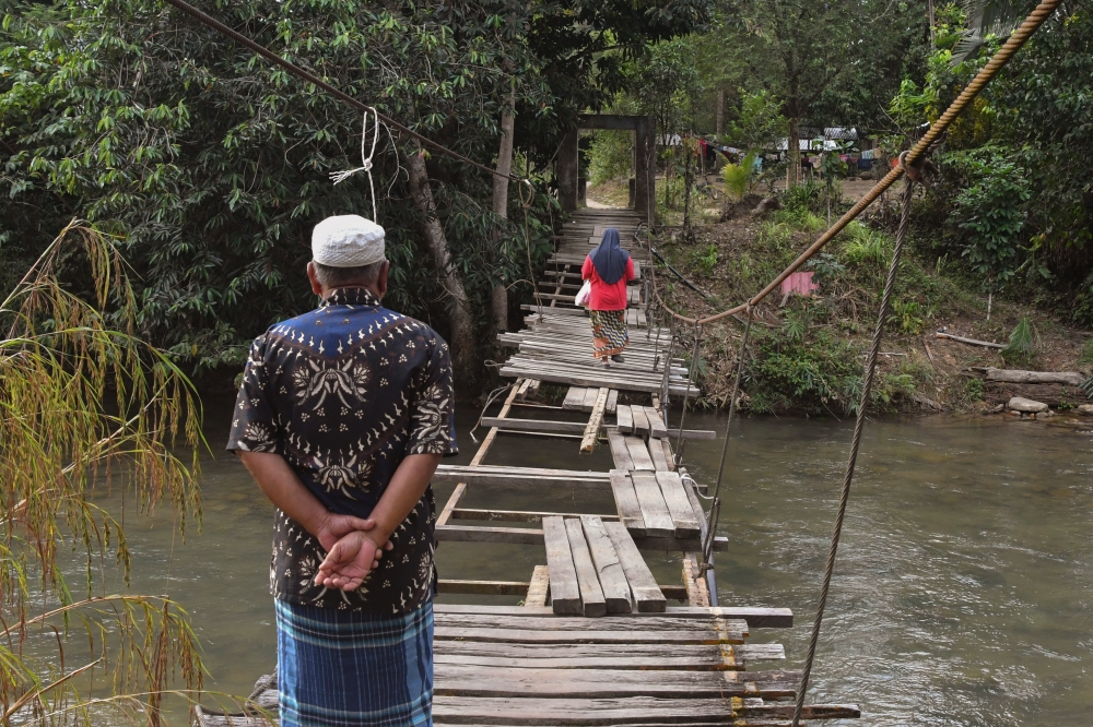 Residents of Kampung Chatel Damai in Lata Rek, Kuala Krai, cautiously use a temporarily repaired suspension bridge while awaiting construction of a new, safer structure. — Bernama pic
