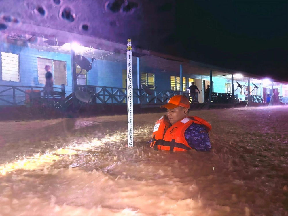 A rescuer wades through floodwaters to assess rising water levels outside a building during overnight flooding, as continuous rain forces evacuations in parts of Sarawak. — Social media pic