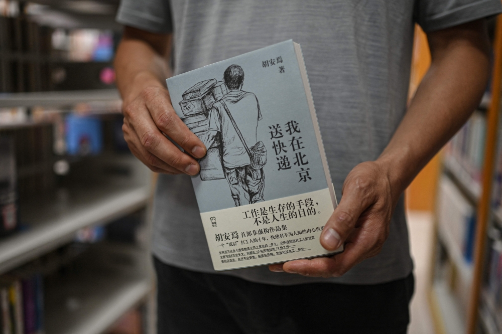 This photo taken on August 18, 2025 shows author Hu Anyan posing for a portrait photo with his book ‘I Deliver Parcels in Beijing’ at a public library in Chengdu, in southwestern China’s Sichuan province. — AFP pic
