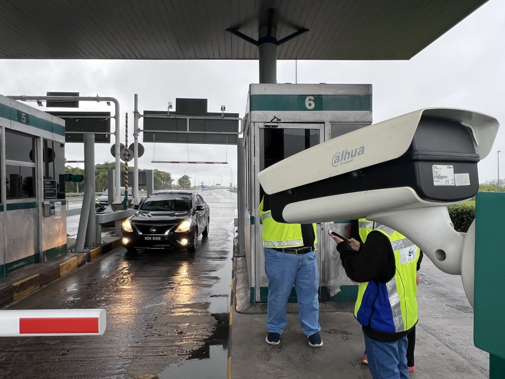 PLUS personnel conduct testing of ANPR cameras at a toll plaza during wet conditions, as part of trials to assess system accuracy under different operating environments. — PLUS Malaysia Berhad pic