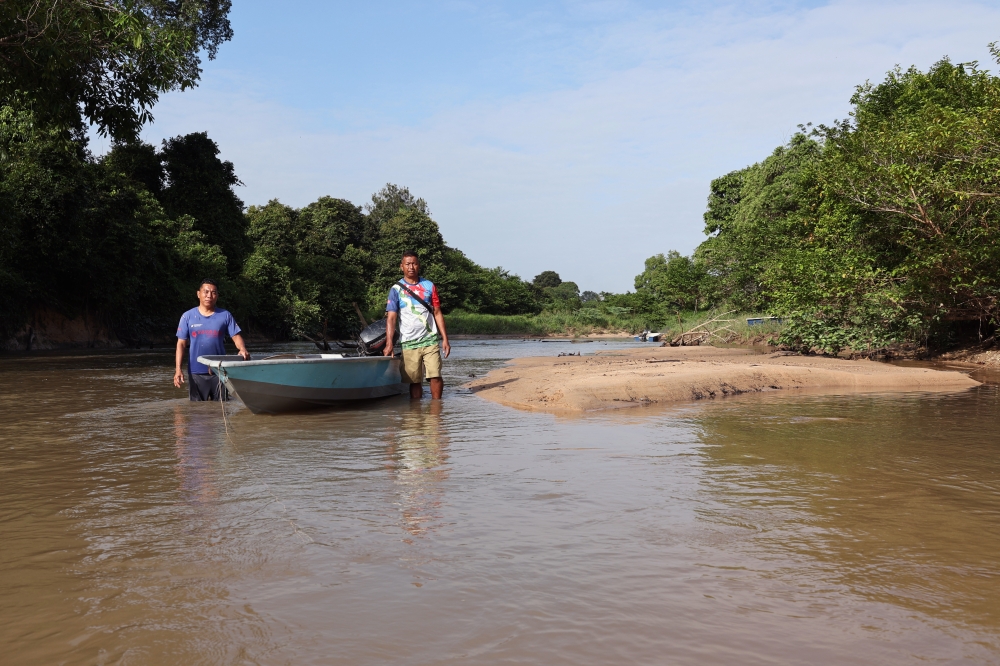 Fishermen Azman Inam (right) and Aris Adong wade through thigh-deep water to move their boat across a newly formed sandbank, a sign, they say, of how much the river has changed since the pollution. — Bernama pic