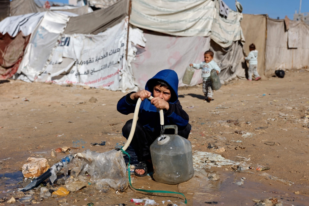 A Palestinian child fills a water container from a hose. — AFP pic