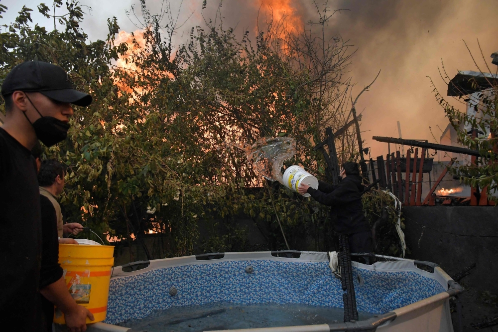 Residents try to extinguish a burning house during a wildfire in Concepcion, Chile, on January 18, 2026. — AFP pic