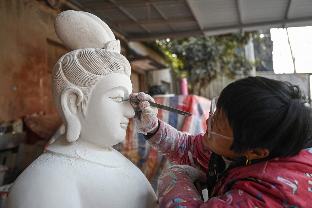 In this picture taken on January 16, 2026, an artisan carves a wooden Bodhisattva sculpture at a workshop at Chongshan village in Suzhou. — AFP pic