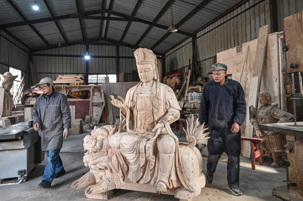In this picture taken on January 16, 2026, two artisans walk past a wooden Buddhist figure sculpture at a workshop at Chongshan village in Suzhou. — AFP pic