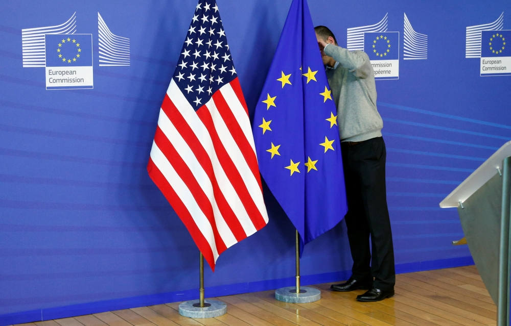 A worker adjusts European Union and US flags at the EU Commission headquarters in Brussels. — Reuters pic