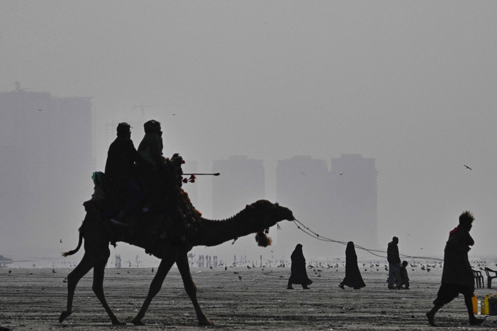 People ride a camel amid dense smog at the Seaview Beach in Karachi January 10, 2026. — AFP pic
