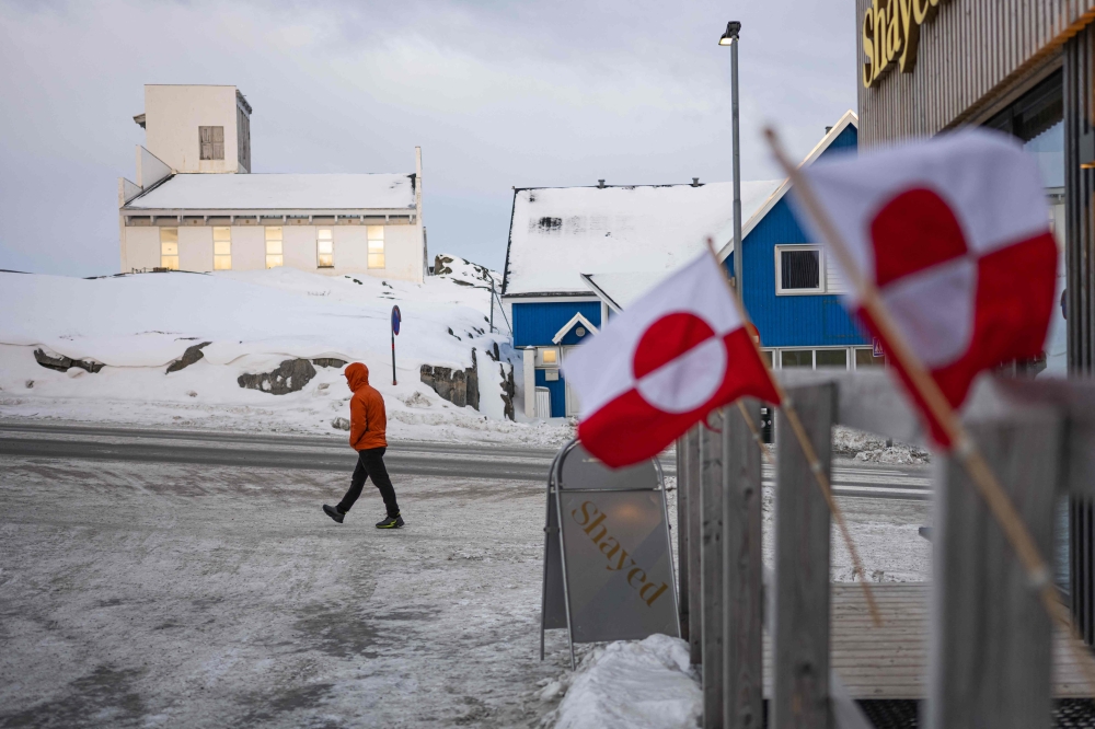 Greenlandic flags are seen in the foreground as a pedestrian walks along a snowy street in Nuuk, Greenland, on January 22, 2026. — AFP pic
