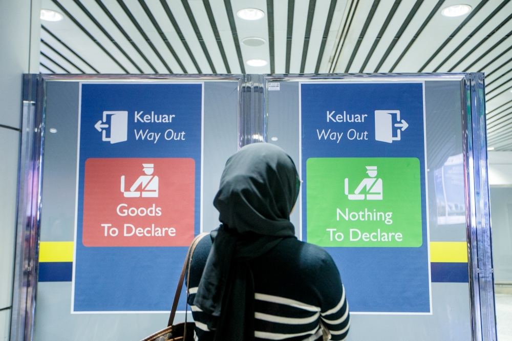 A traveller stands in front of sign indicating the red and green lanes for customs clearance at the Kuala Lumpur International Airport on January 26, 2026. — Picture by Raymond Manuel